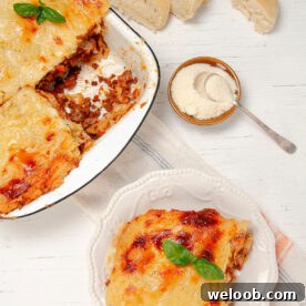 Slice of Lasagna on a plate with a bowl of freshly baked lasagna on the side.