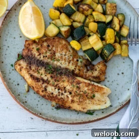 Lemon pepper tilapia on a plate with sautéed zucchini.