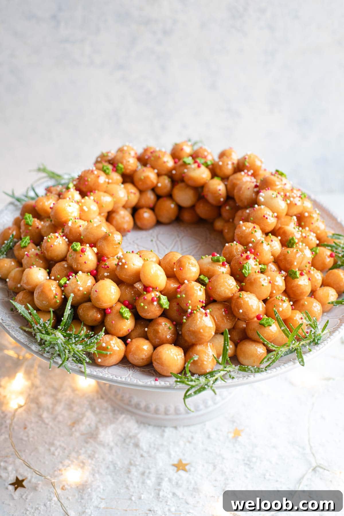 A side shot of Italian struffoli (honey balls) on a cake stand topped with sprinkles