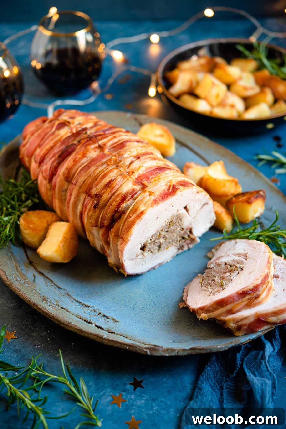 A stuffed turkey breast on a serving plate with slices cut and roasted potatoes