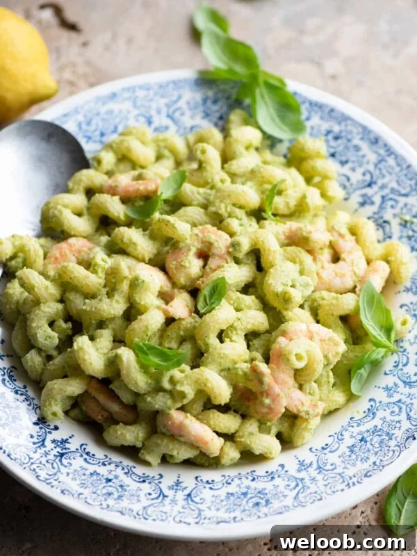 Zucchini shrimp pasta salad in a blue and white bowl topped with basil leaves.