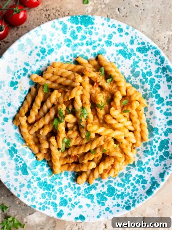 Pasta in a tuna tomato sauce in a blue and white spotted plate sitting on a travertine surface.