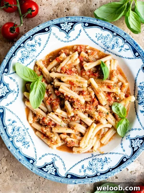 A blue and white vintage bowl with pasta in a fresh tomato sauce topped with basil. The bowl is on a travertine surface with cherry tomatoes and basil around.