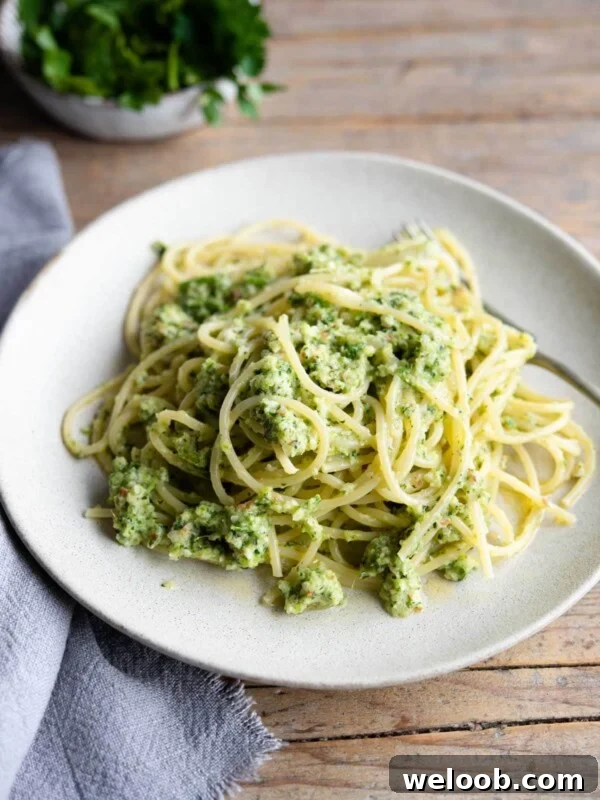A plate for zucchini pesto pasta on a wooden surface with a blue towel at the side