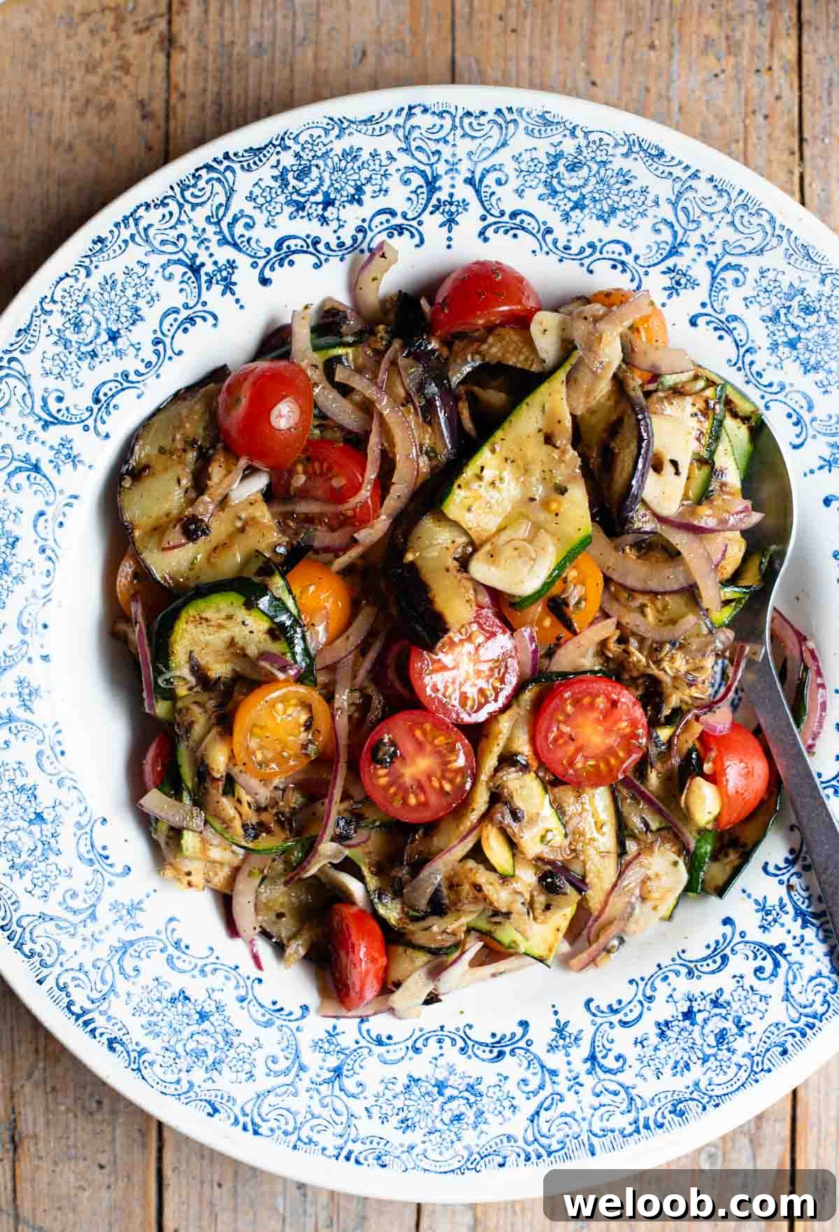 An overhead shot of marinated grilled summer vegetables in a blue bowl on a wooden surface.