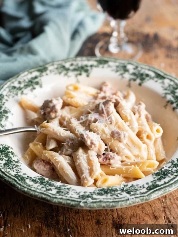 Pasta alla Norcina in a green and white bowl with a fork and glass of wine in the background.