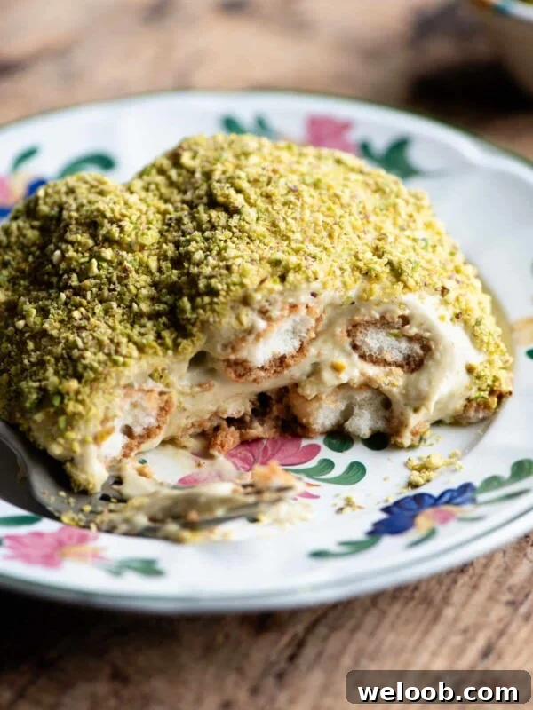 A close up of a piece of pistachio tiramisu on a plate sitting on a wooden table.