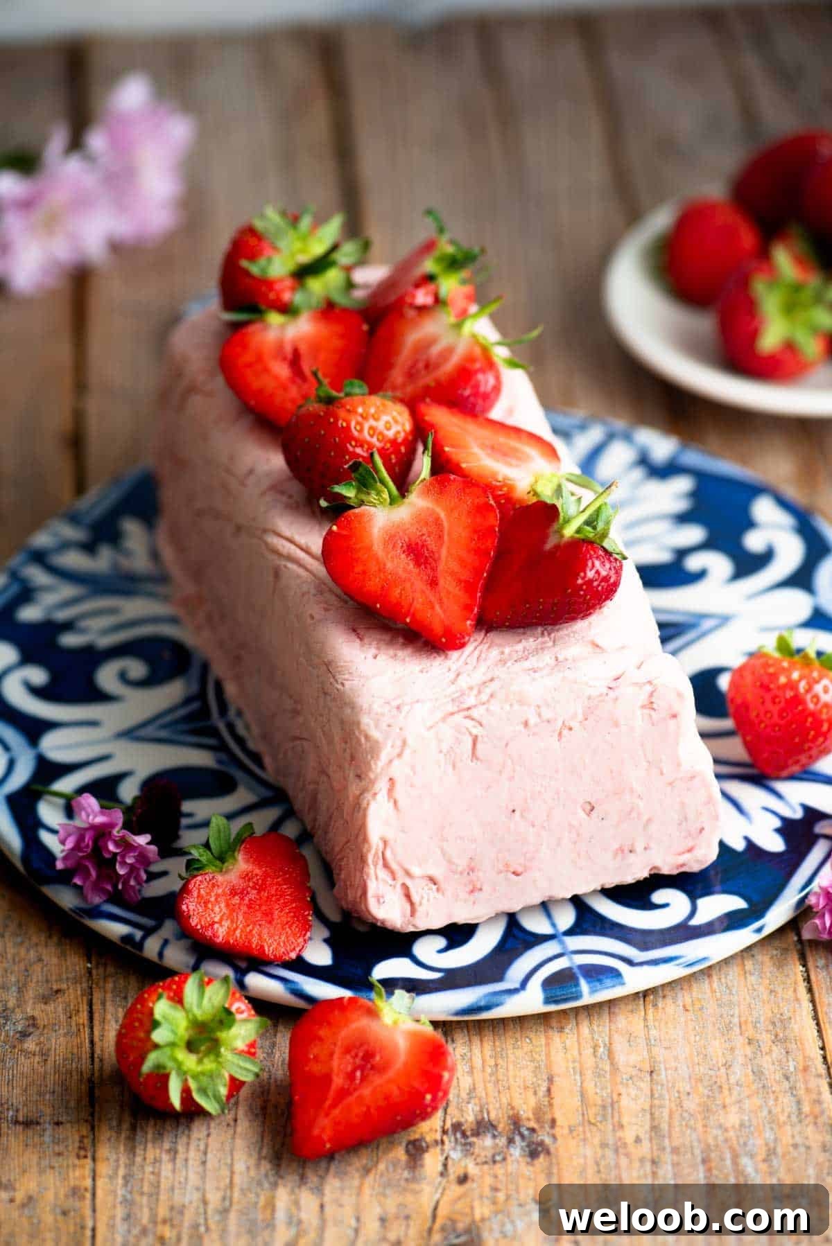 Silky Strawberry Semifreddo with Fresh Strawberry Sauce 2 Strawberry semifreddo on a blue and white ceramic serving board topped with cut strawberries.