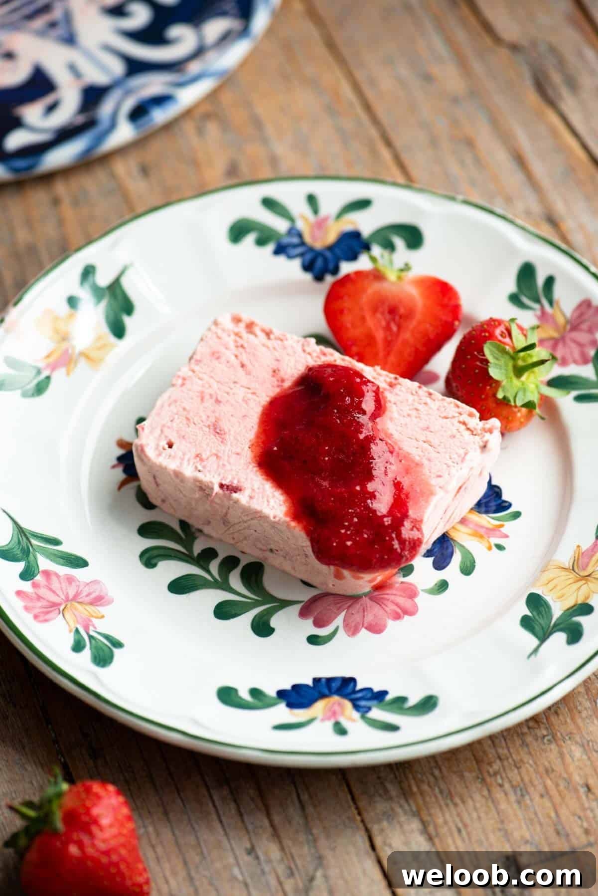 Silky Strawberry Semifreddo with Fresh Strawberry Sauce 4 A slice of strawberry semifreddo on a floral plate topped with strawberry sauce.