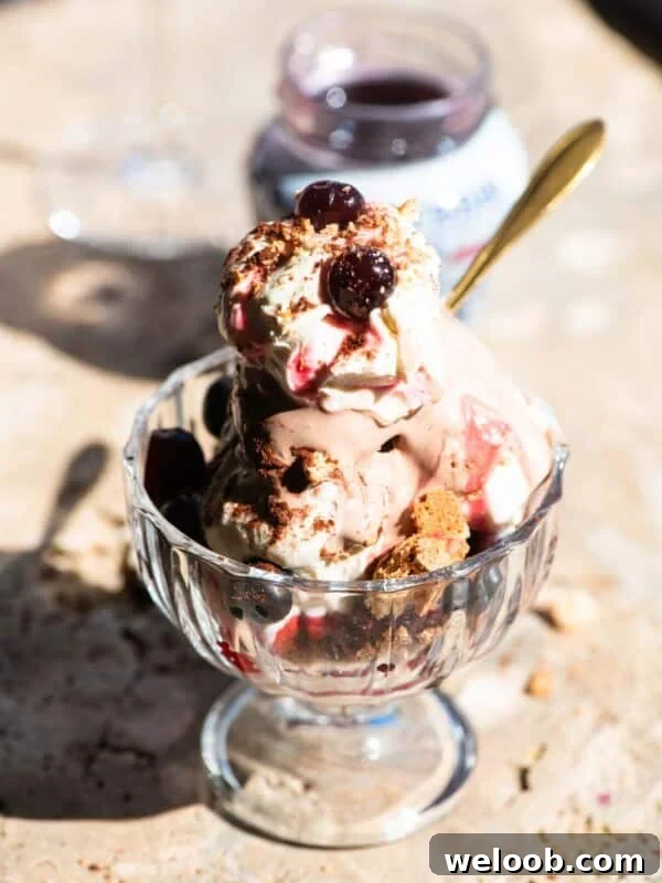 Silky Strawberry Semifreddo with Fresh Strawberry Sauce 8 An Italian ice cream sundae in a glass bowl with cream and cherries on top sitting on a travertine surface.