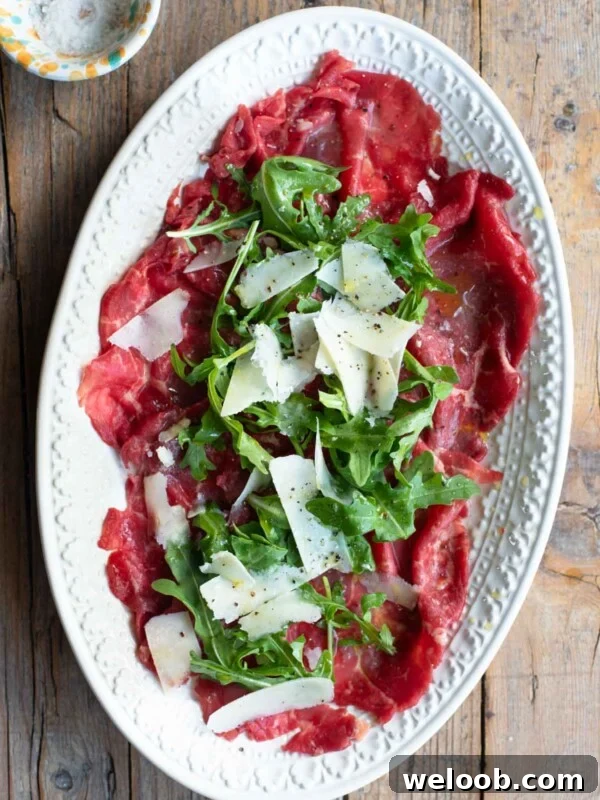 Beef Tramezzino with Radicchio, Cheese and Porchetta 6 An overhead shot of beef carpaccio on a white oval serving plate topped with arugula and Grana Padano cheese.