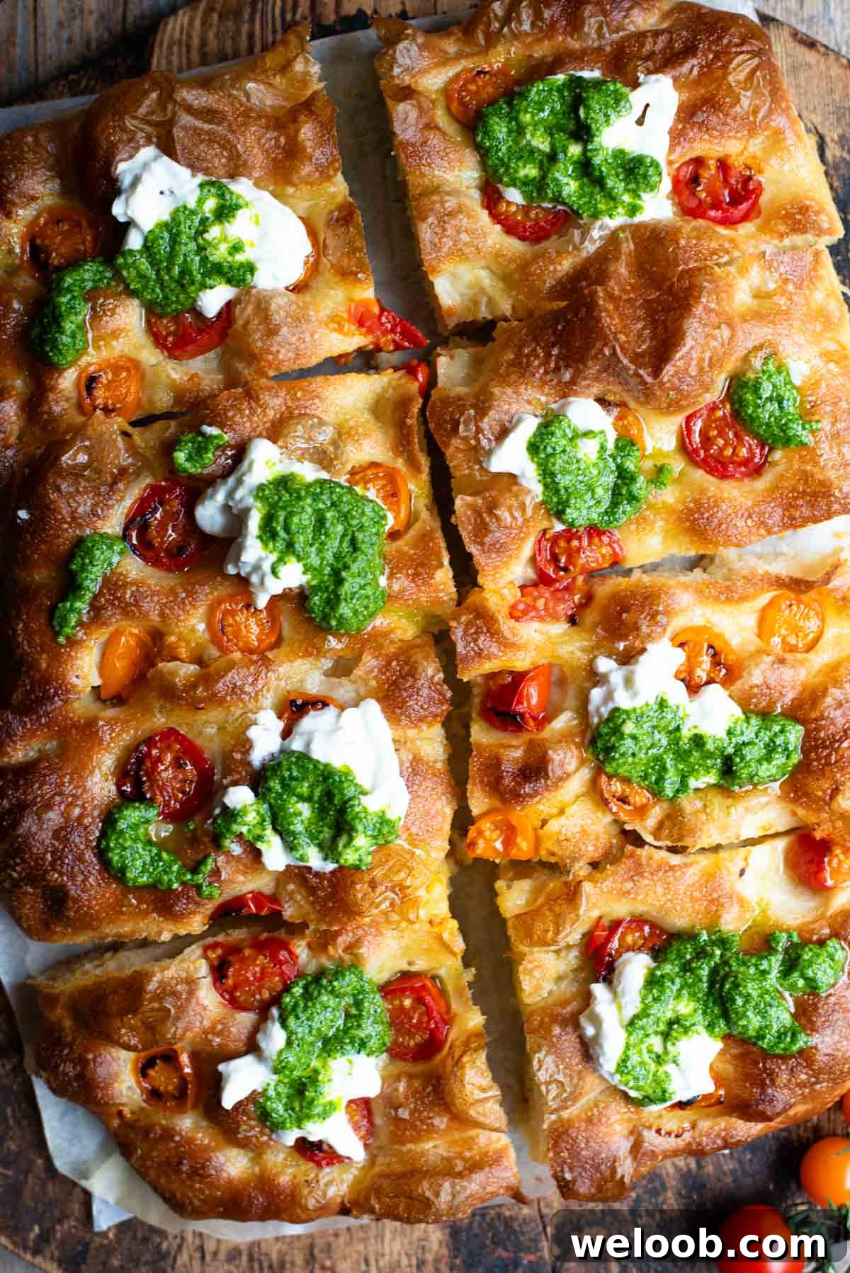 Crispy Roasted Tomato Focaccia with Pesto and Burrata 2 An overhead shot of a focaccia cut into 8 slices and topped with cherry tomatoes, pesto and burrata.