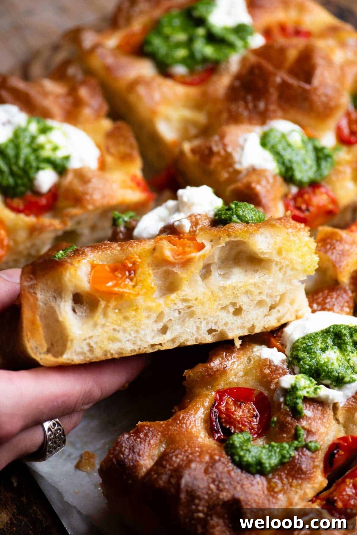 Crispy Roasted Tomato Focaccia with Pesto and Burrata 4 A close up of a hand holding a slice of focaccia showing the airy and light texture inside.