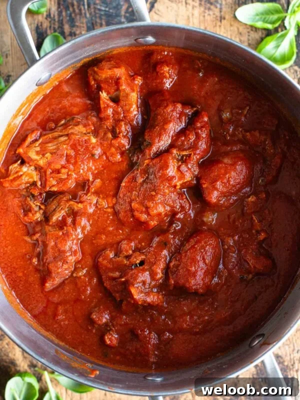 An overhead shot of Sugo Napoletano (Neapolitan ragu) in a large pot sitting on a wooden surface.