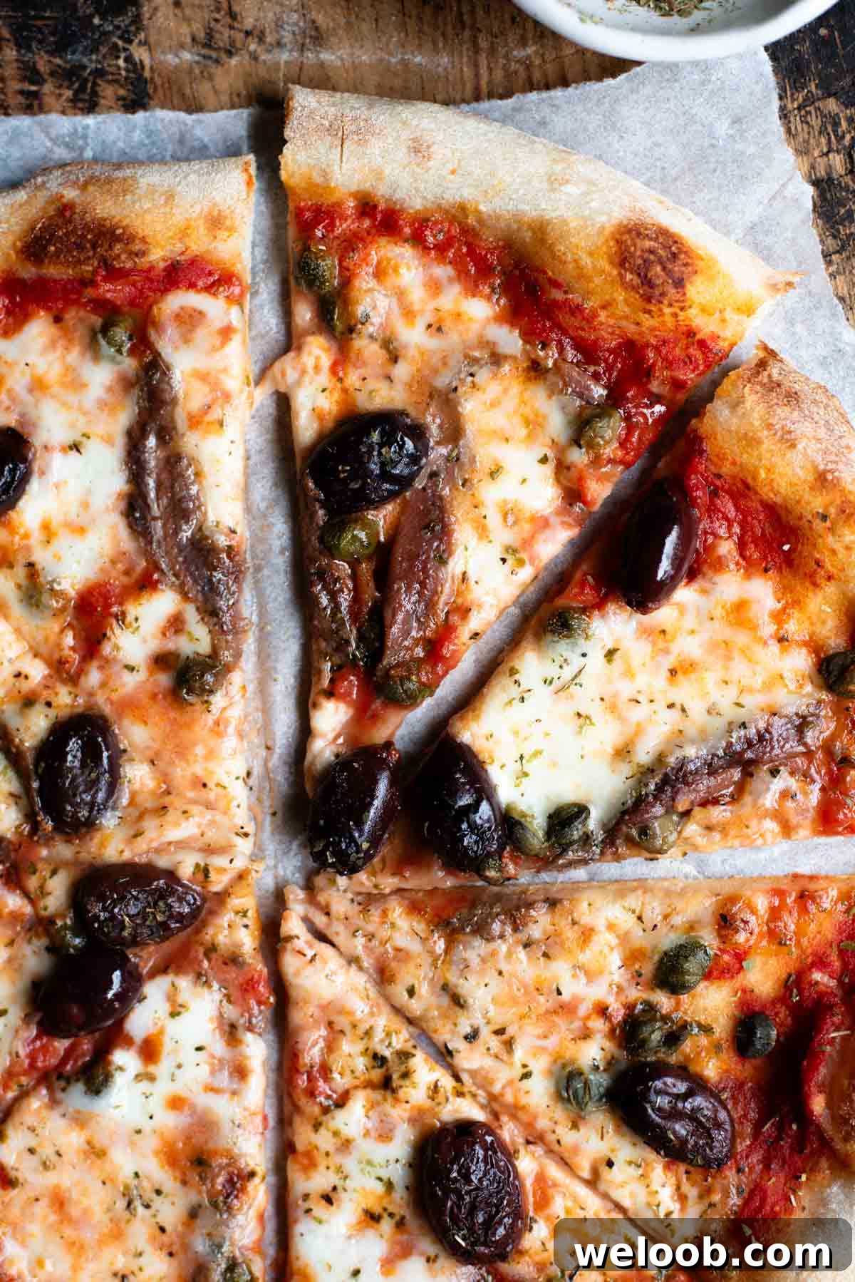 Mediterranean Olive, Anchovy and Caper Pizza with Oregano 4 A close up of slices of pizza with mozzarella, tomato, olives, capers and anchovies.