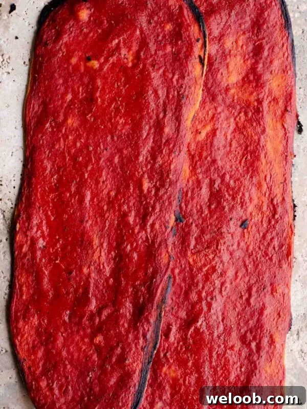Mediterranean Olive, Anchovy and Caper Pizza with Oregano 7 Two long thin and crispy pizzas covered in tomato sauce sitting on a travertine surface.