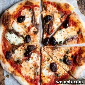 Mediterranean Olive, Anchovy and Caper Pizza with Oregano 9 A close up of a pizza cut into slices topped with olives, capers ad anchovies.