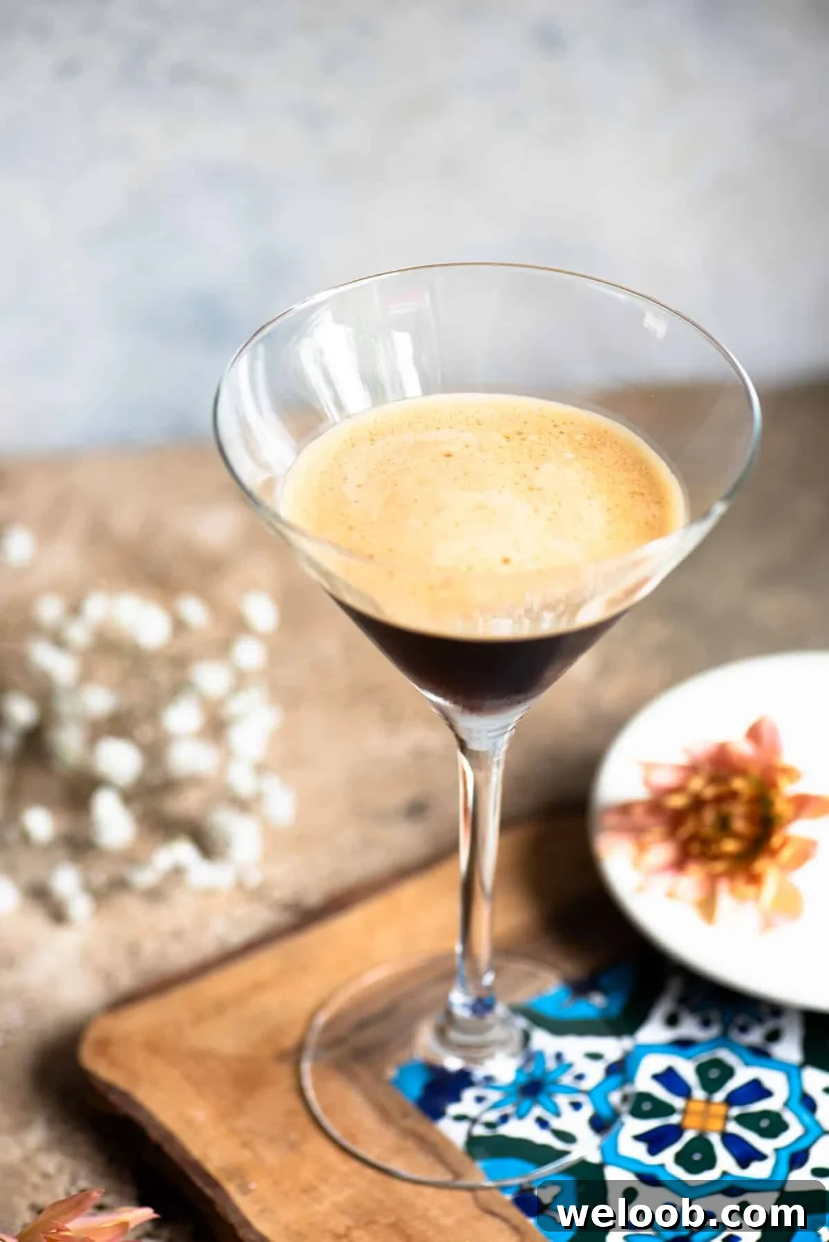 Caffè Shakerato: Classic Italian Iced Coffee Recipe 3 A martini glass filled with an iced coffee on a patterned tile with flowers at the side.