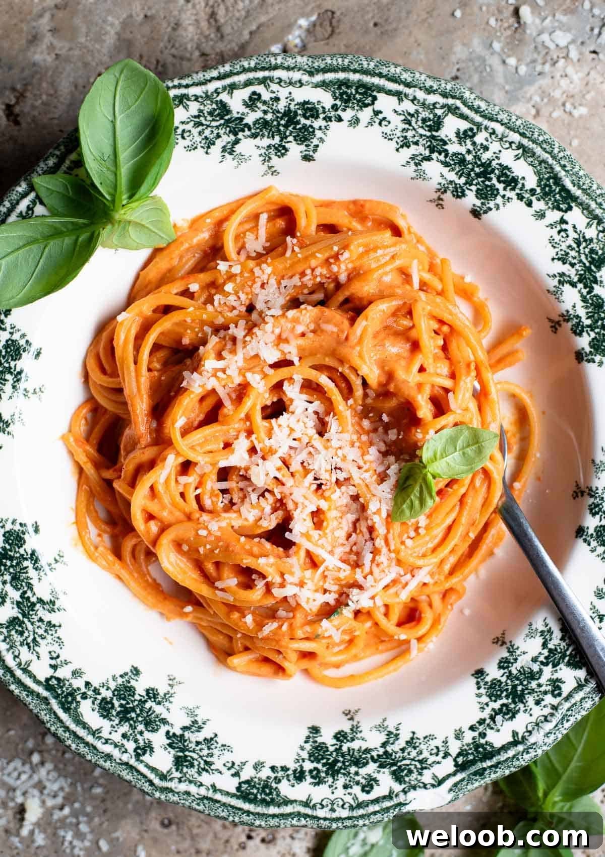 Creamy Ricotta Pasta with Roasted Cherry Tomatoes 2 An overhead shot of roasted cherry tomato and ricotta spaghetti in a green floral bowl with basil scattered around.