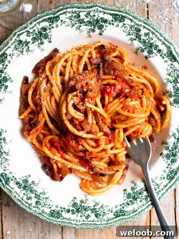 An overhead shot of spaghetti in a green and white vintage style bowl with a tomato and pancetta sauce.