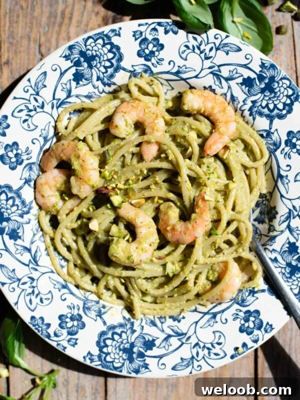An overhead shot of pistachio pasta with shrimp in a blue floral bowl on a wooden background.