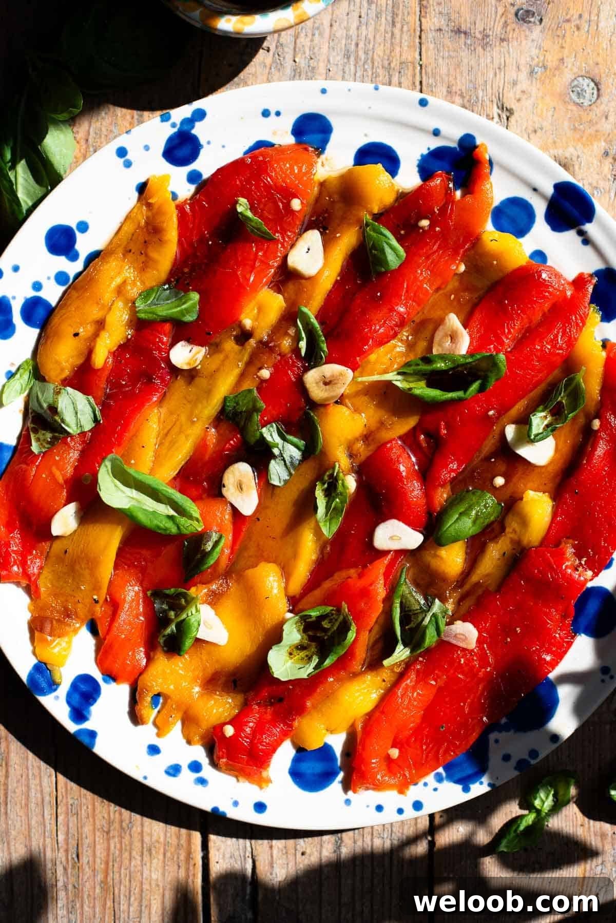 How to Make Italian Marinated Roasted Bell Peppers 2 Red and yellow marinated roasted peppers arranged on a blue speckled plate topped with garlic and basil.