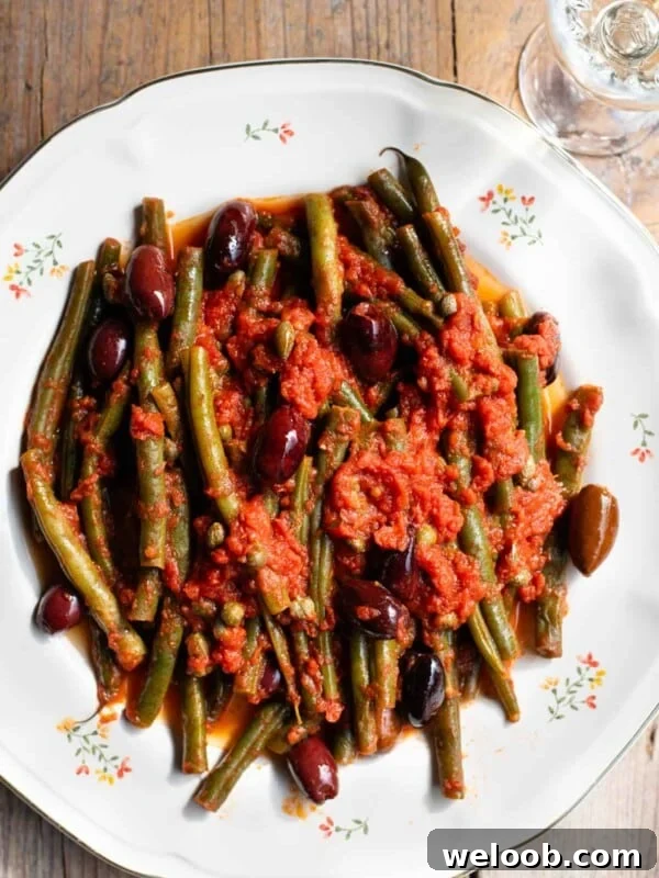 How to Make Italian Marinated Roasted Bell Peppers 7 A close up of green beans in tomato sauce with olives and capers on a white floral plate and rustic wooden background.