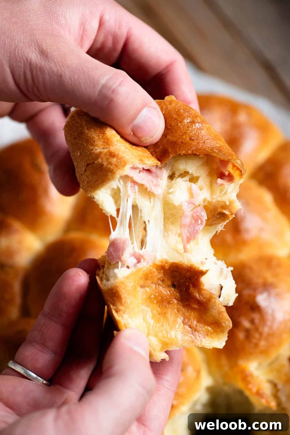 A hand tearing open a piece of danubio salato to show the cheese pull and ham inside.