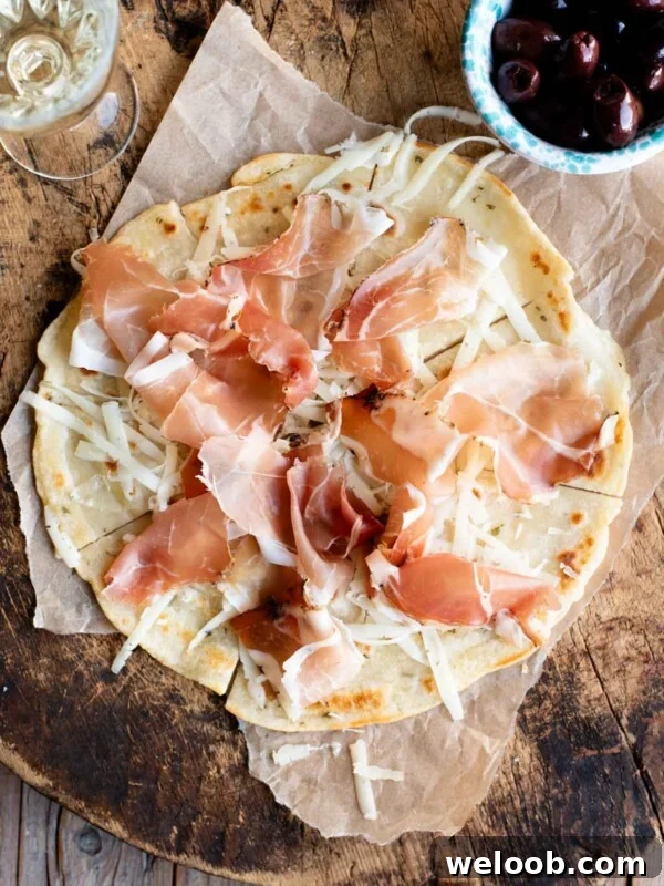 An overhead shot of Brustengo, an Italian flatbread topped with cured meat and cheese on a wooden board.